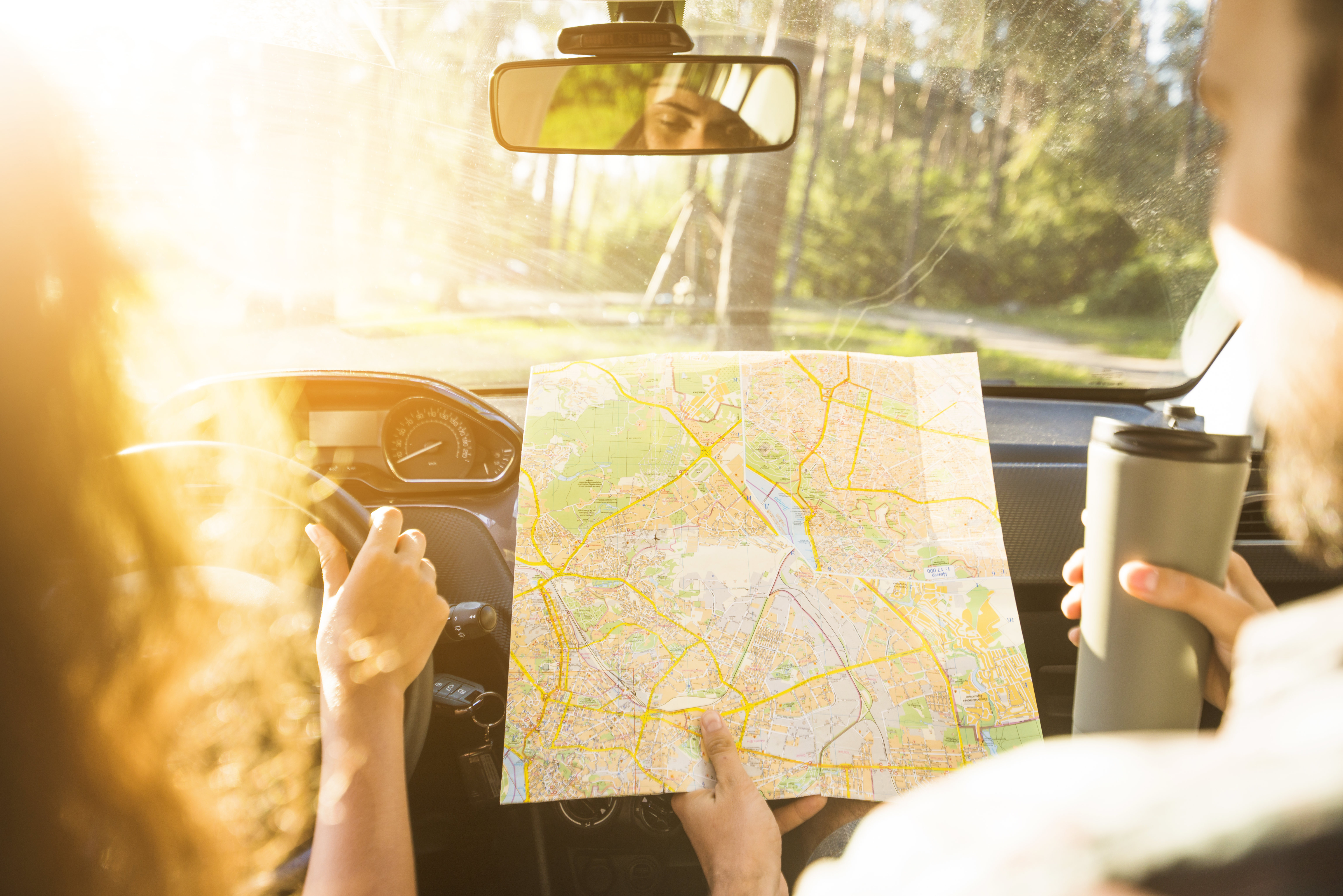 Passenger holding a paper map while driver sets off on a road trip through countryside